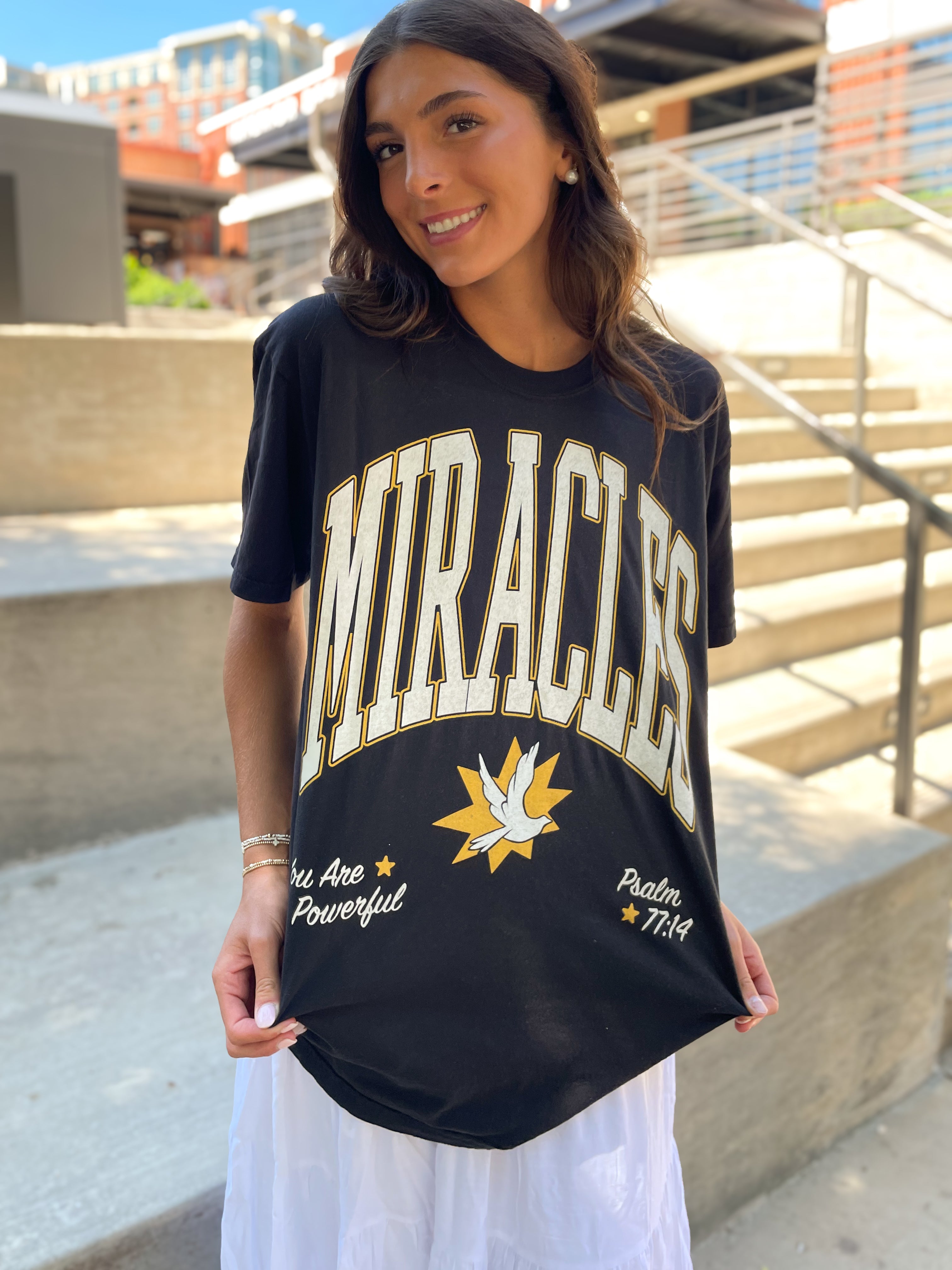 a woman holding a black t - shirt with the word,'miracles'on
