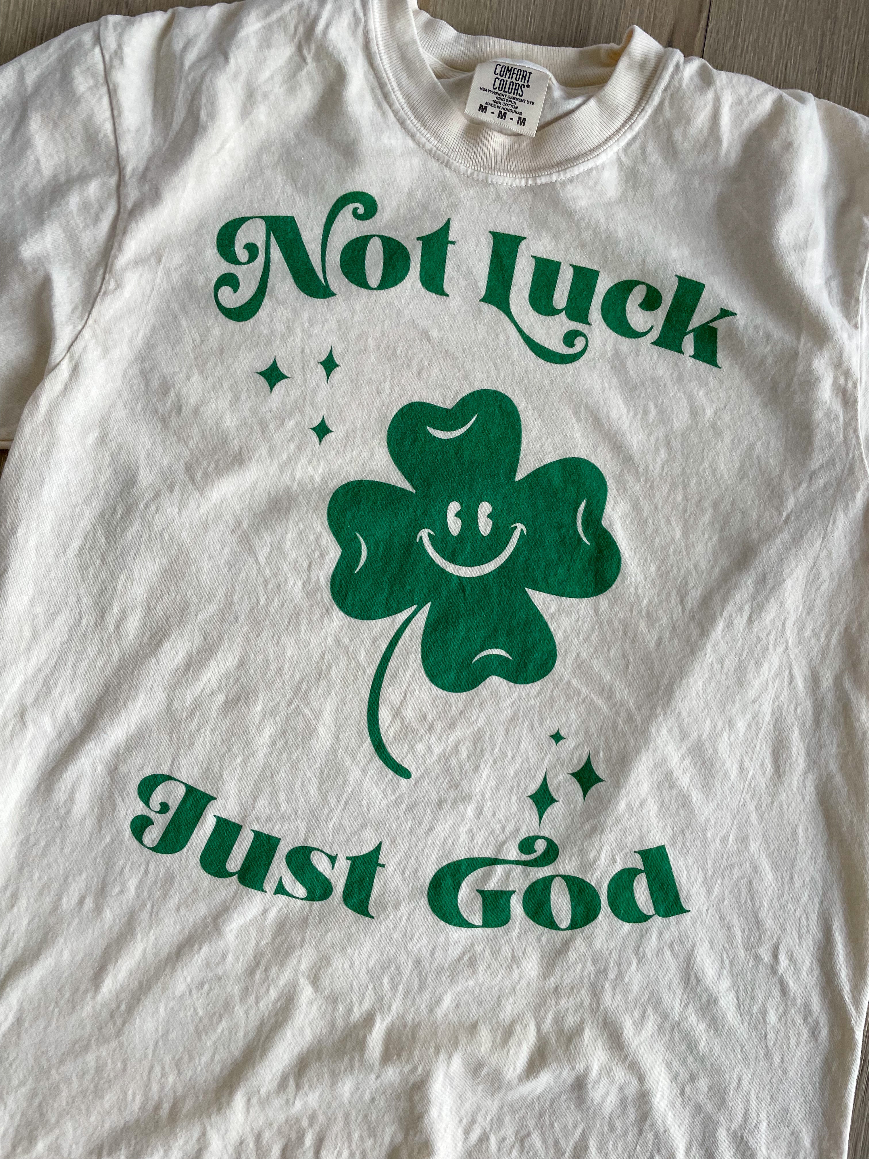 a white t - shirt with a shamrock saying not luck just god