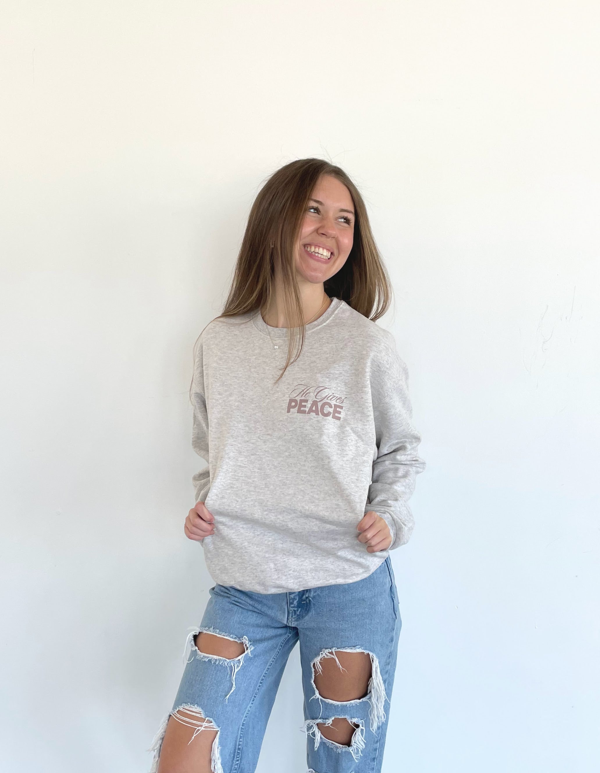 a woman wearing a peace sweatshirt and ripped jeans