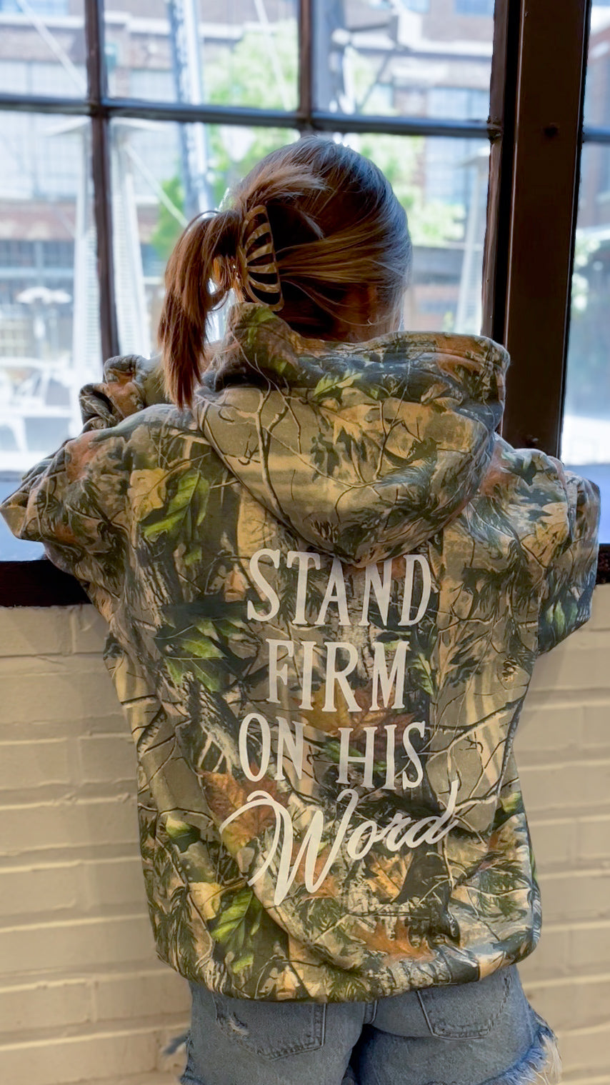 a woman standing in front of a window wearing a camouflage jacket
