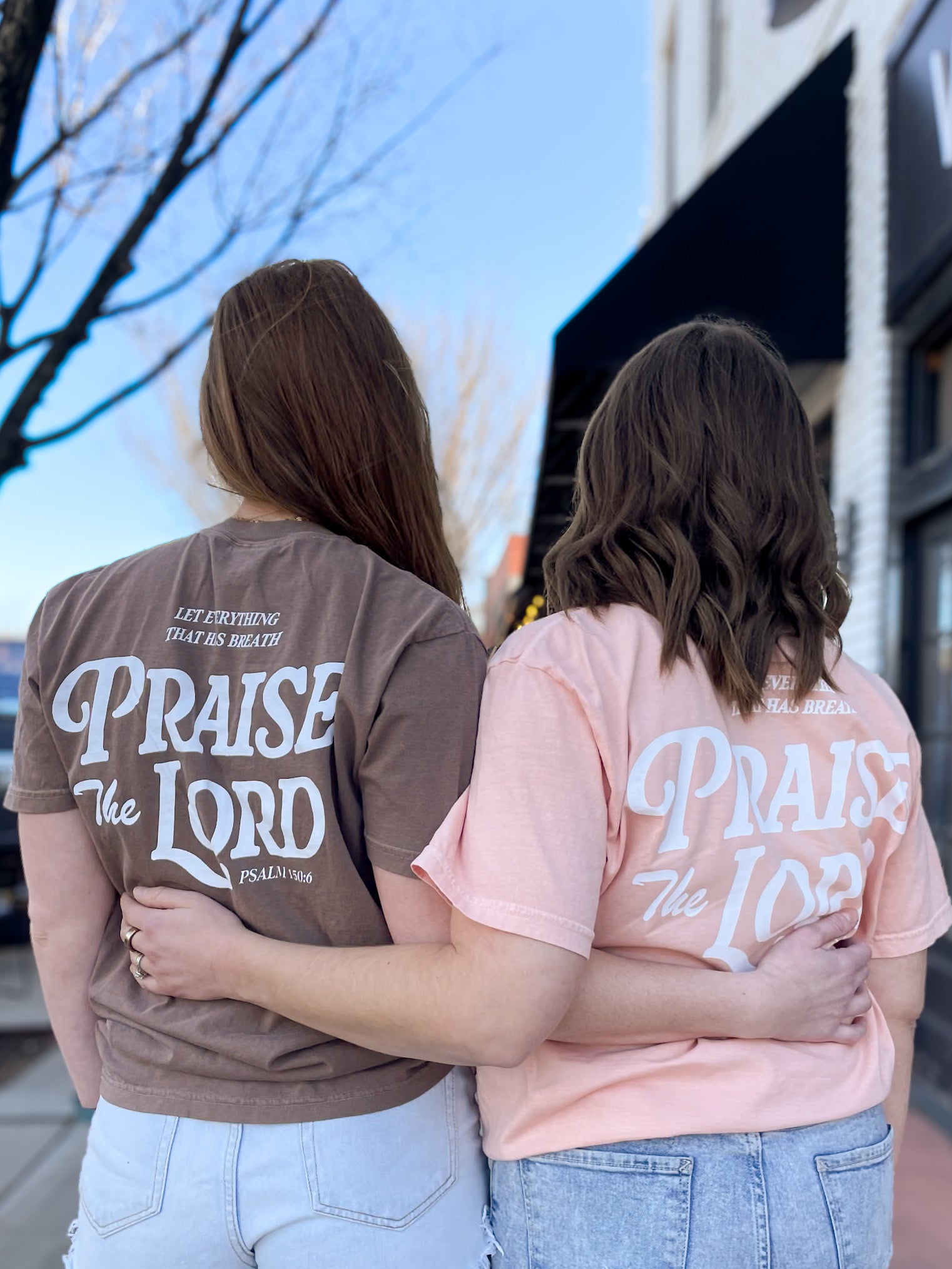 two women standing next to each other in front of a building