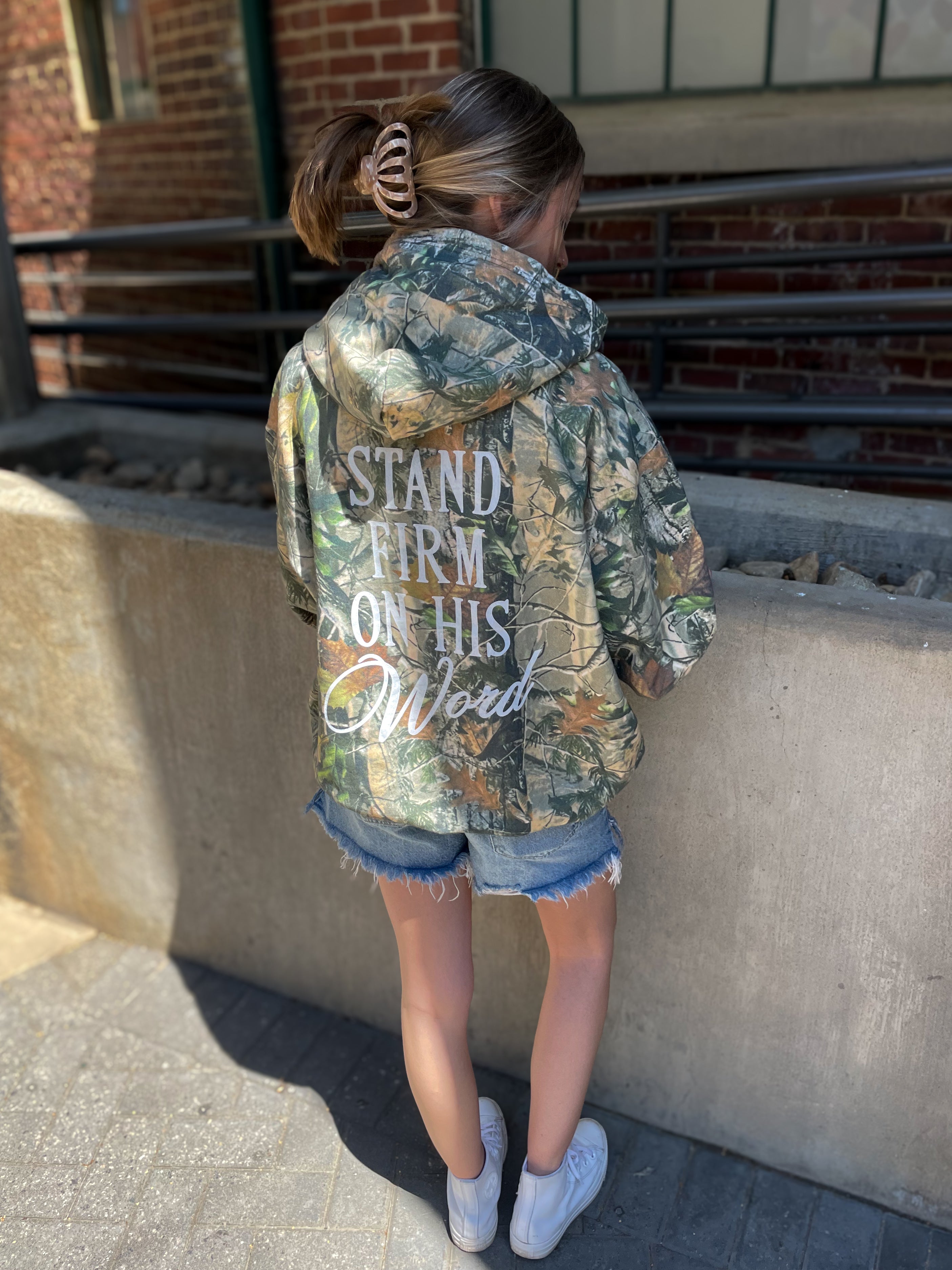 a young girl wearing a camouflage jacket and denim shorts