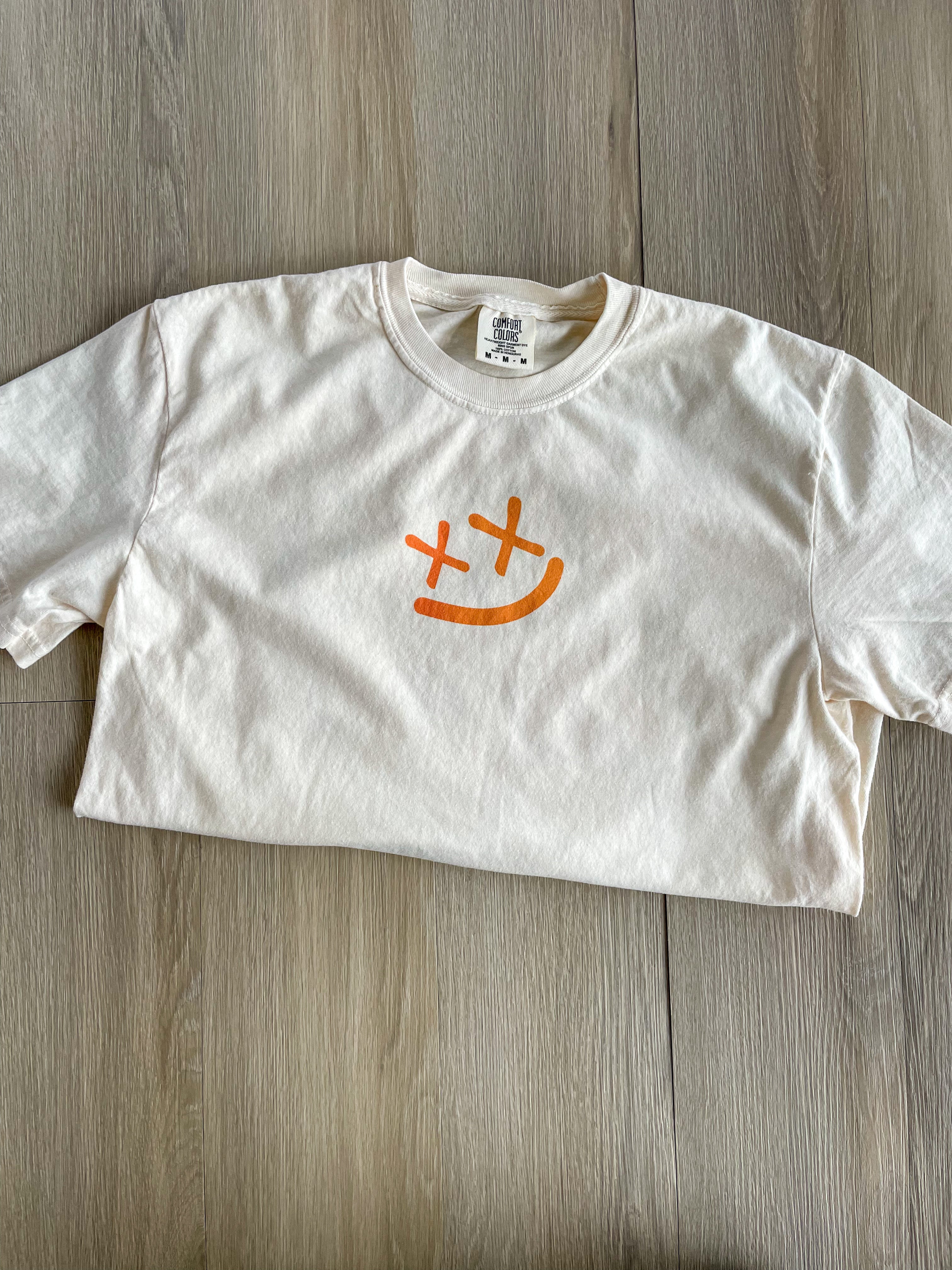 a white t - shirt with an orange smiley face on it