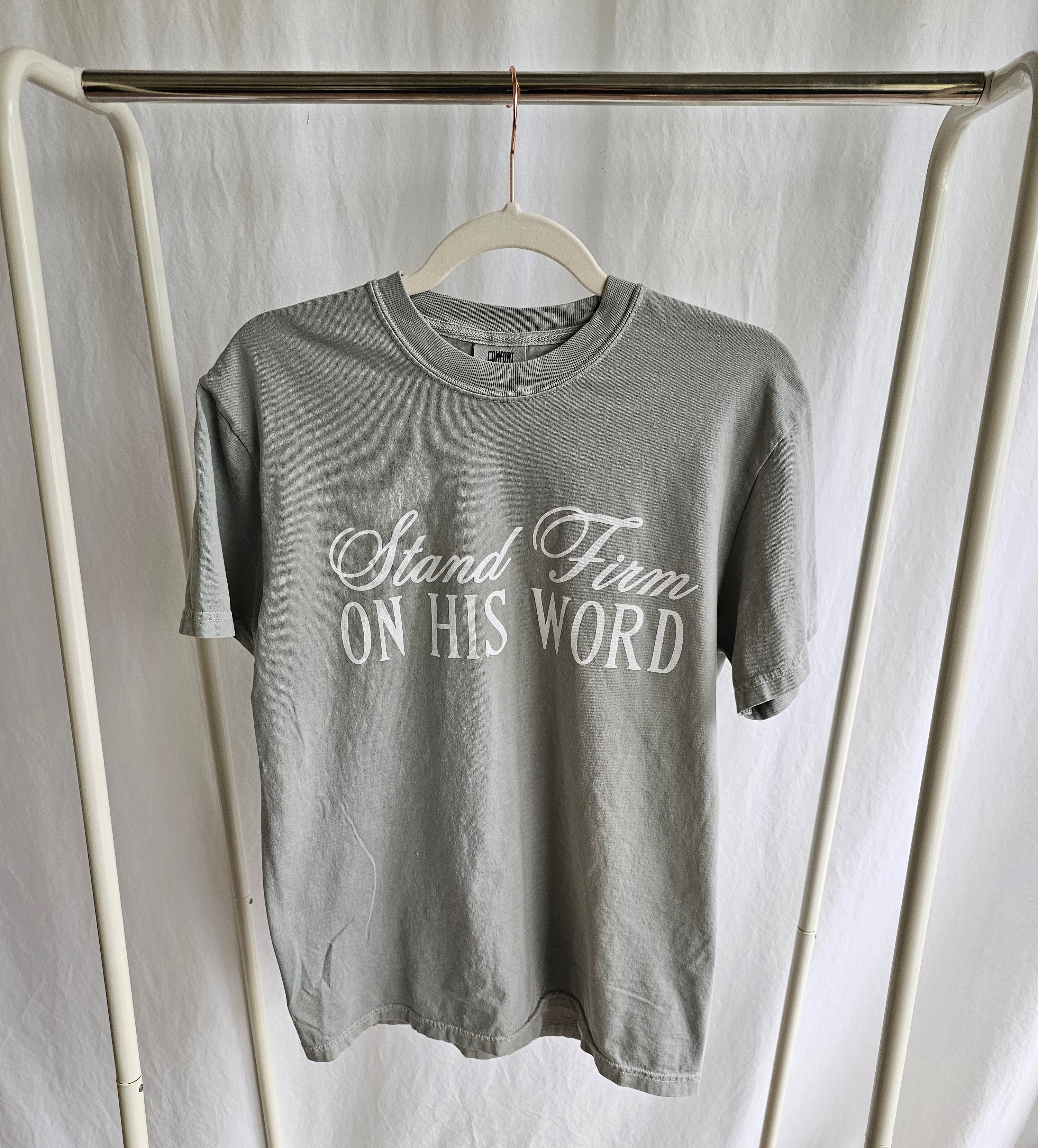 a t - shirt that says stand firm on his word on a hanger