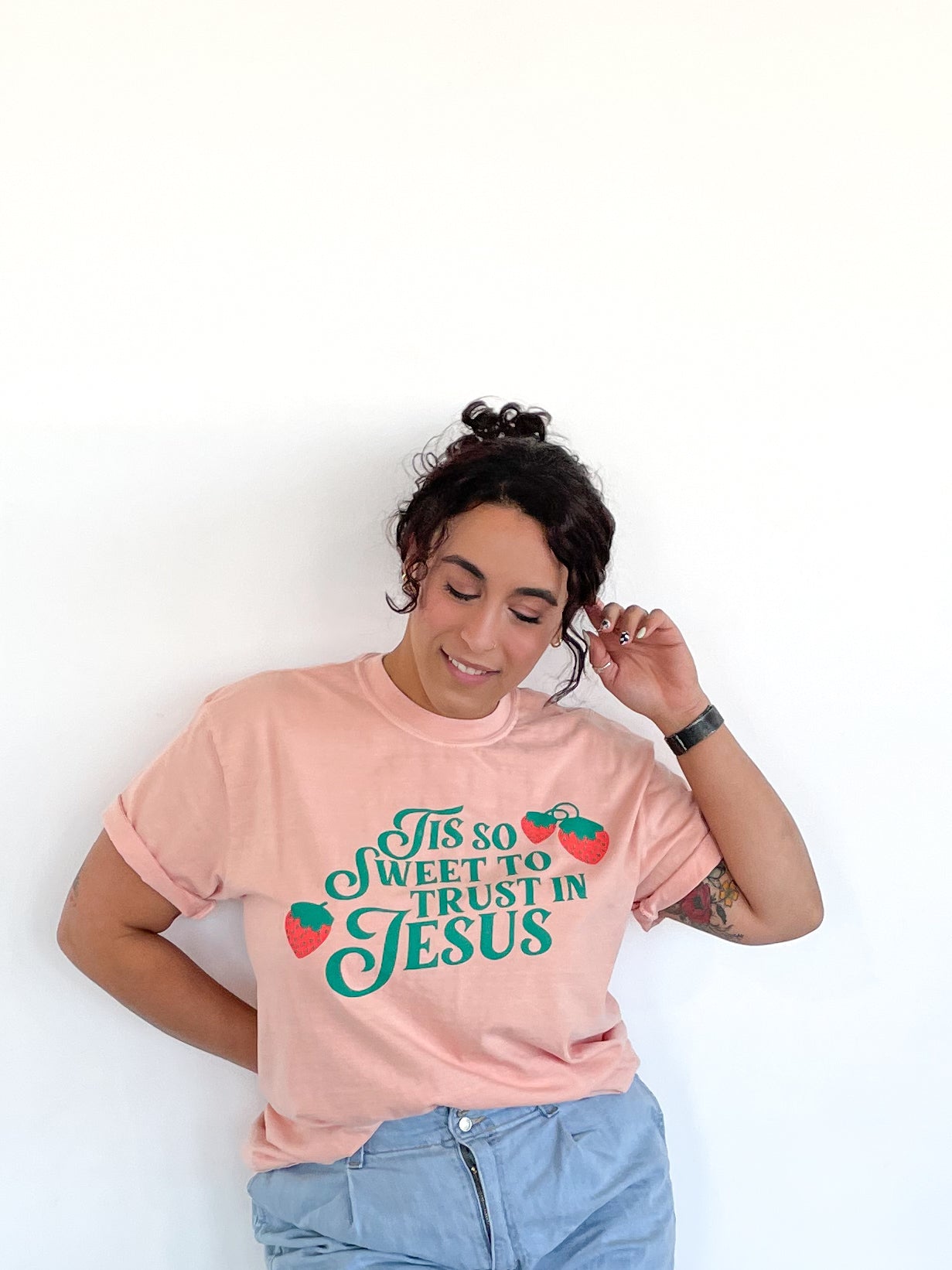 a woman leaning against a wall wearing a pink shirt