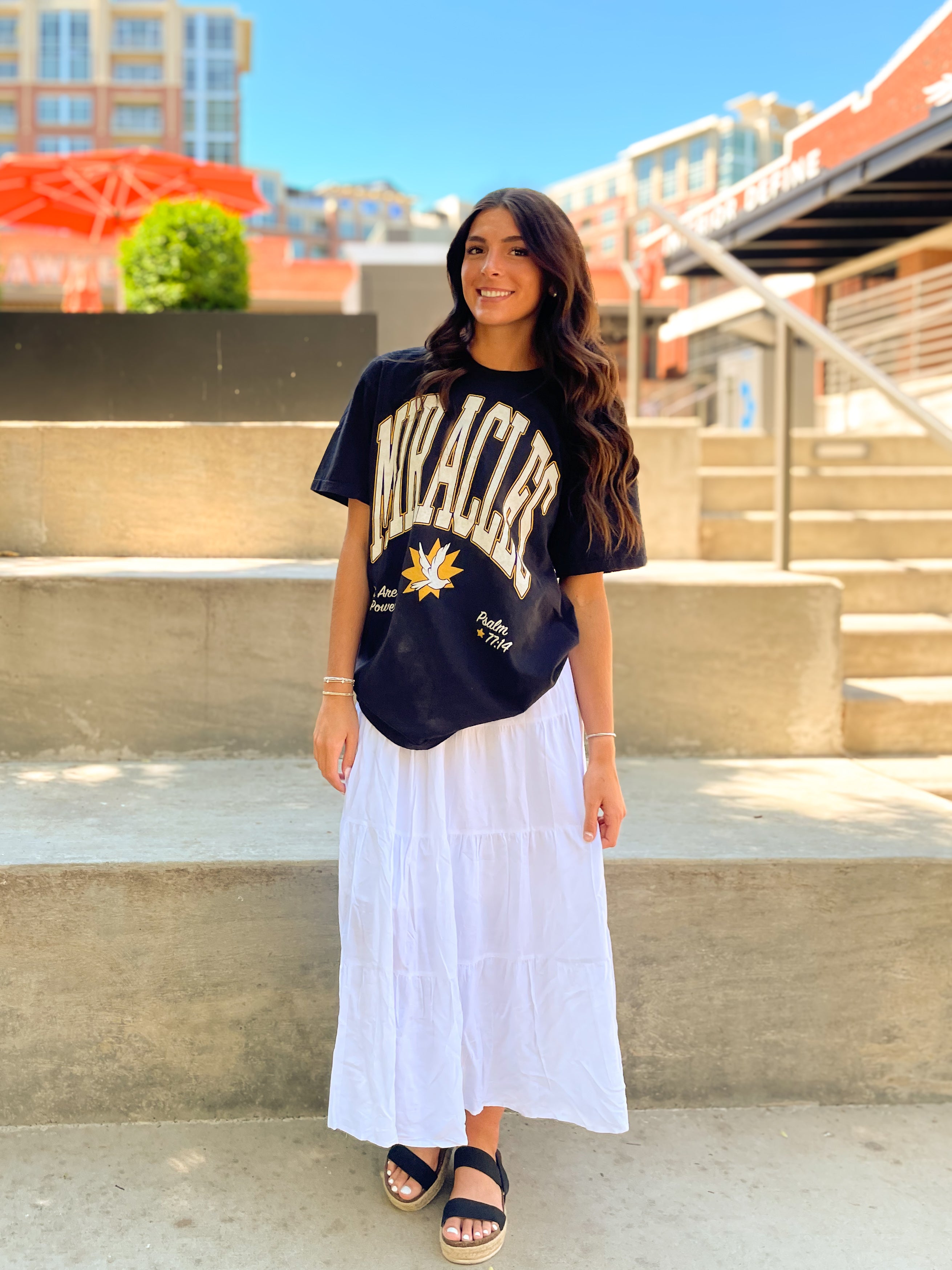 a woman wearing a black and white t - shirt and a white skirt