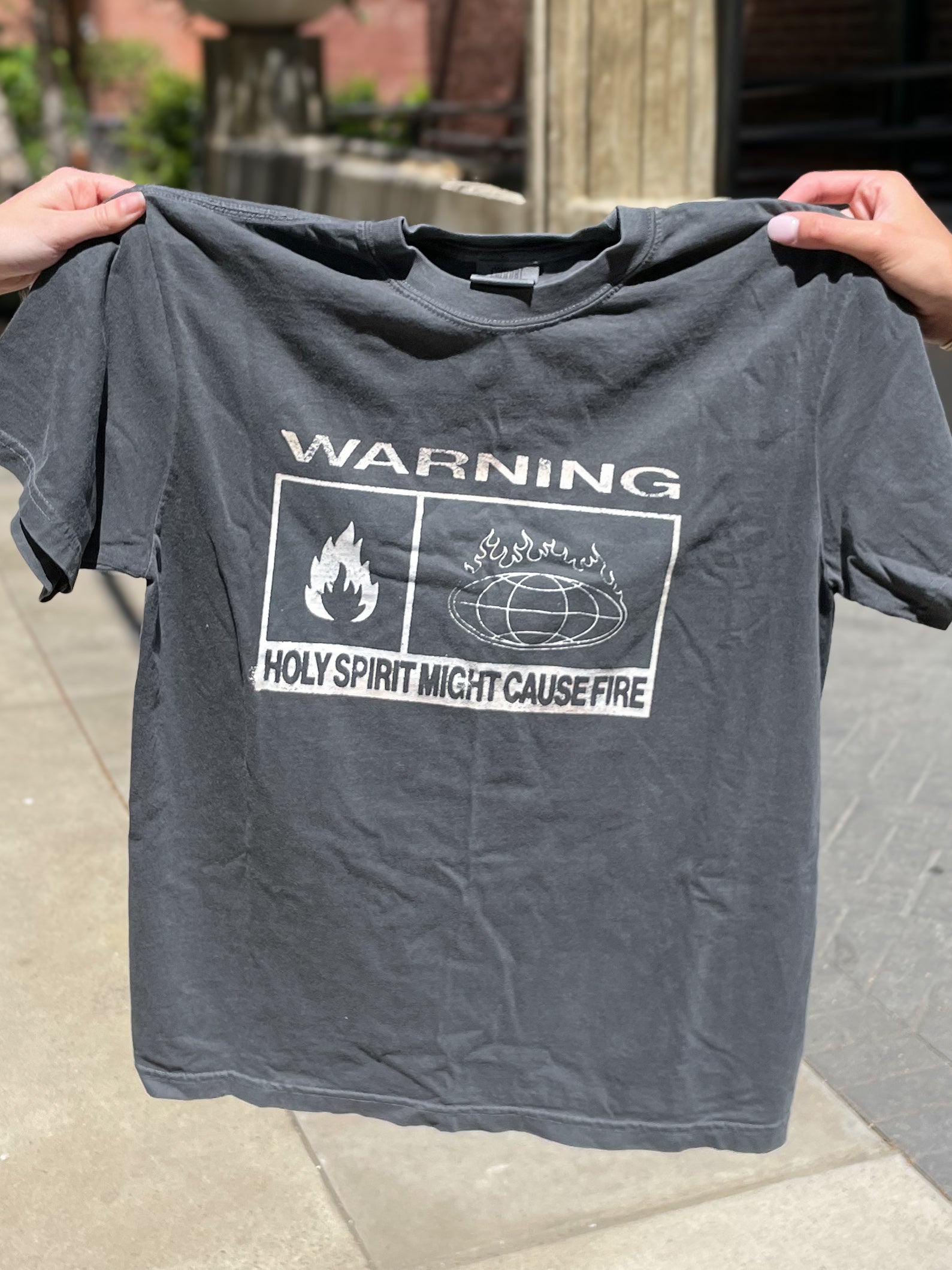 a person holding up a t - shirt that says warning holy spirit might cause fire