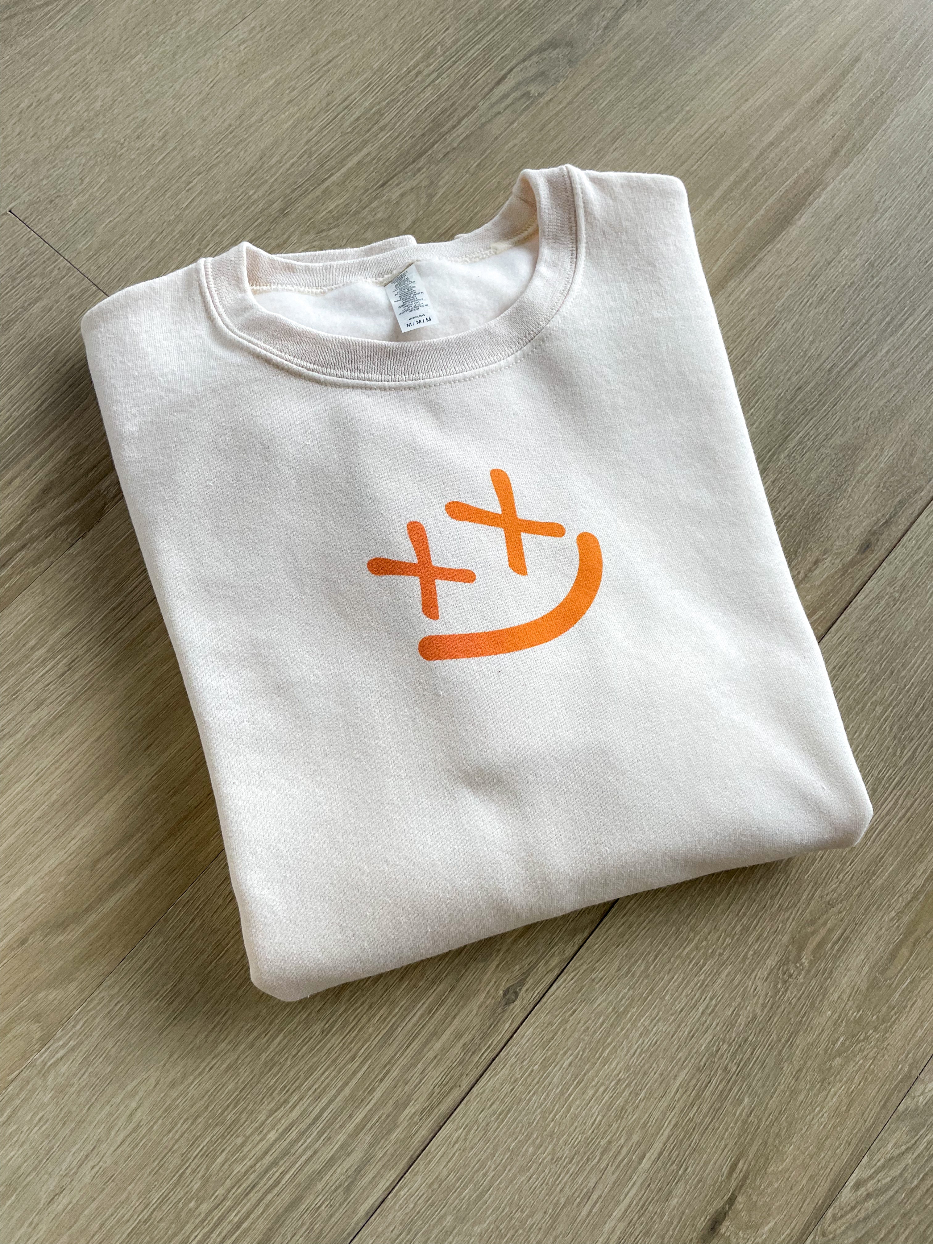 a white t - shirt with an orange smiley face on it