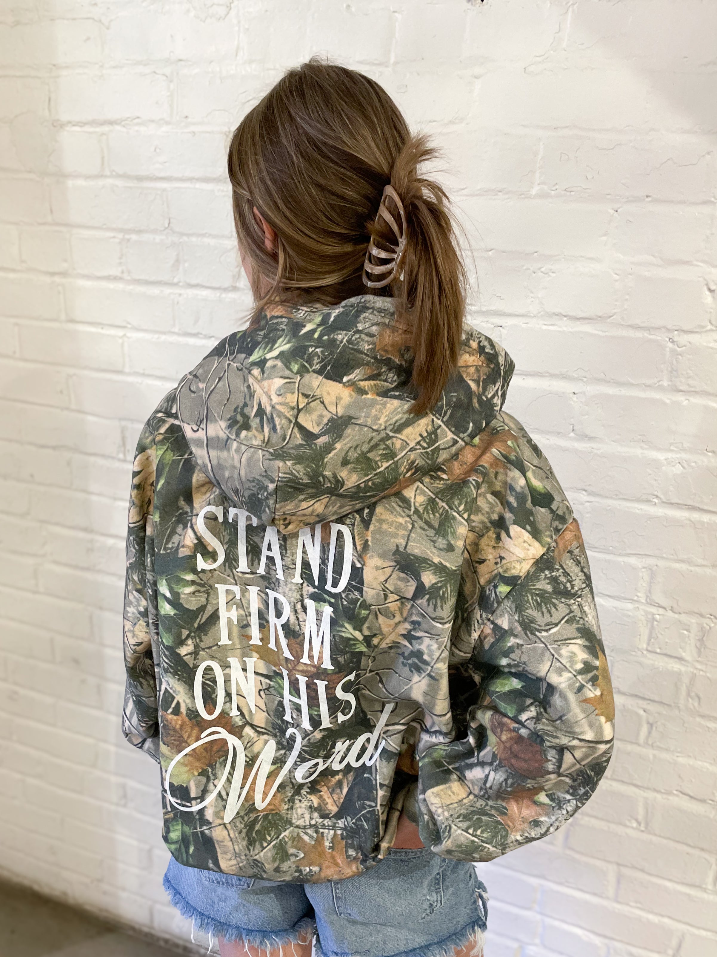 a woman wearing a camouflage jacket with the words stand firm on it