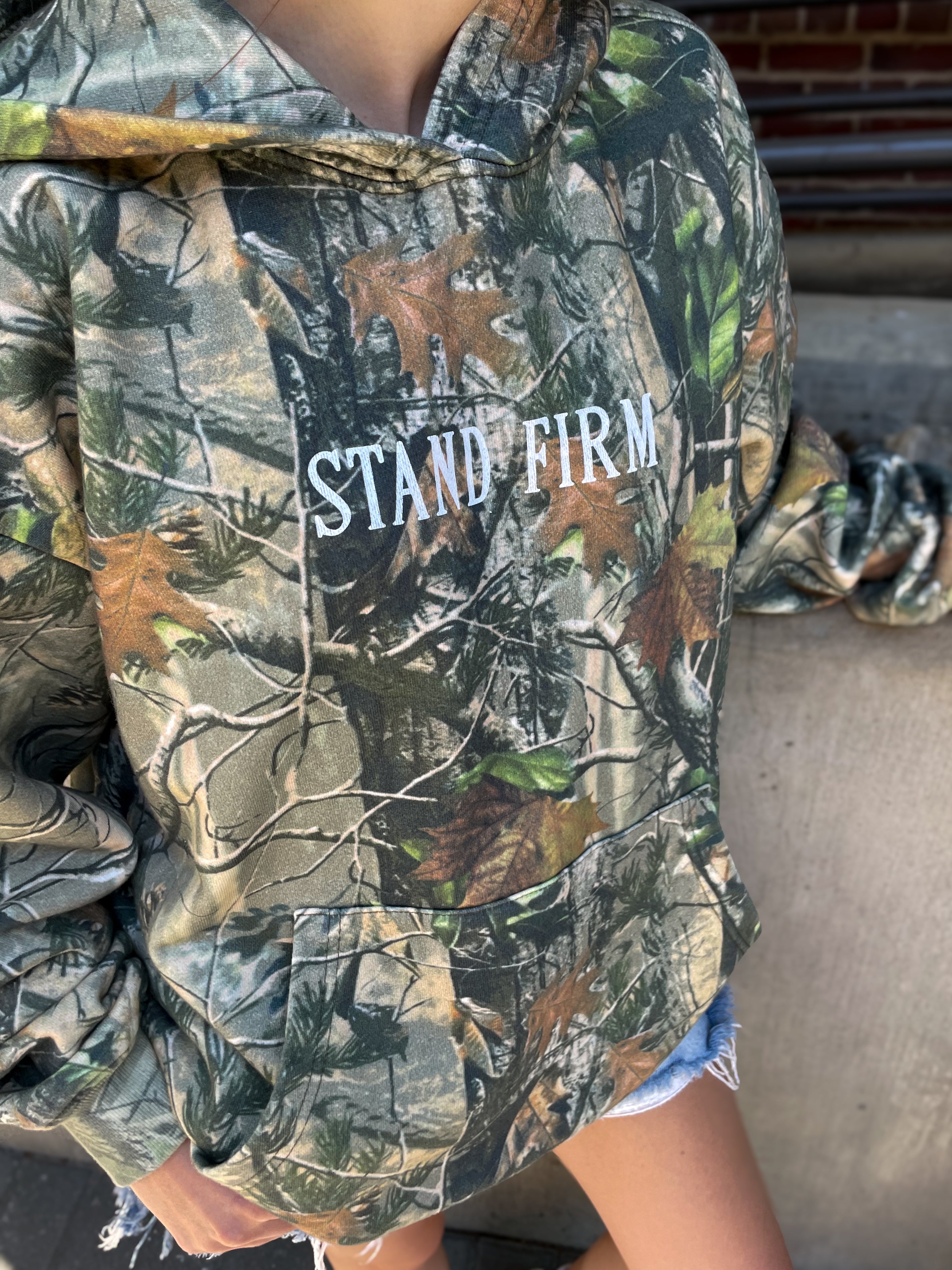 a person wearing a camouflage jacket with the words stand firm on it
