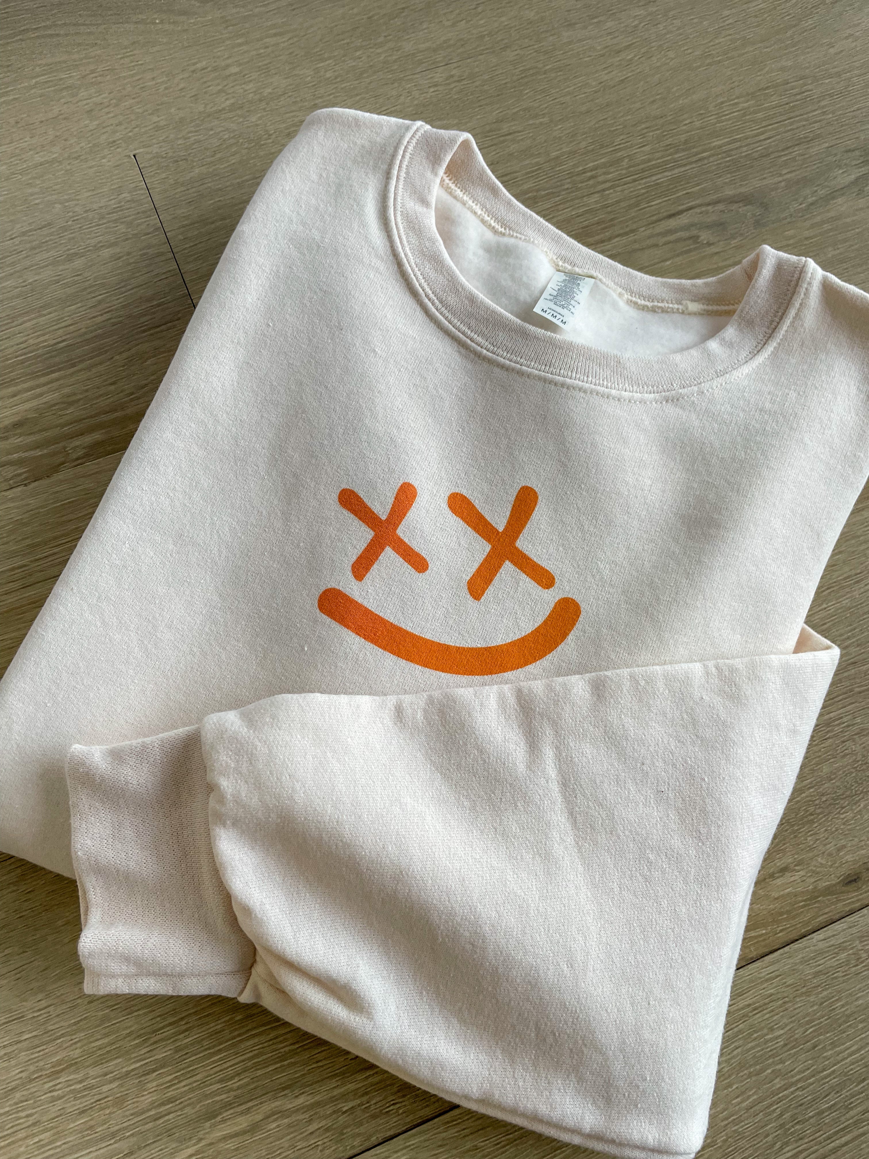 a white shirt with an orange smiley face on it